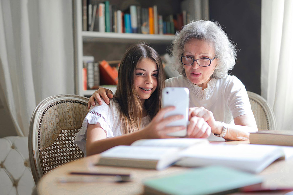 Oma mit Enkeltochter sitzen am Tisch und lesen das digitale Amtsblatt am Handy